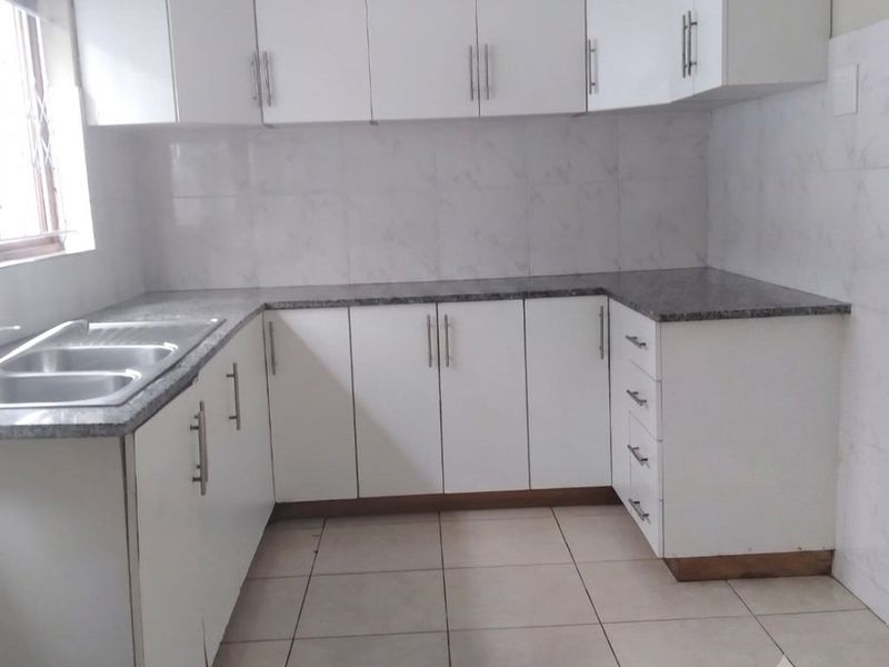 A clean, functional kitchen featuring white cabinetry, granite countertops, a double bowl sink, and tiled flooring.