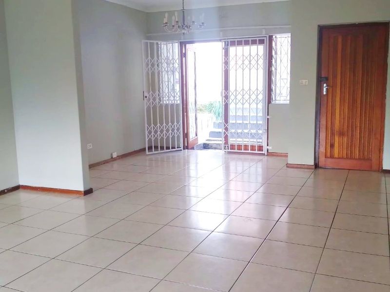A spacious, empty living area featuring neutral tiled flooring, a classic chandelier, and a secure entrance leading to the exterior.