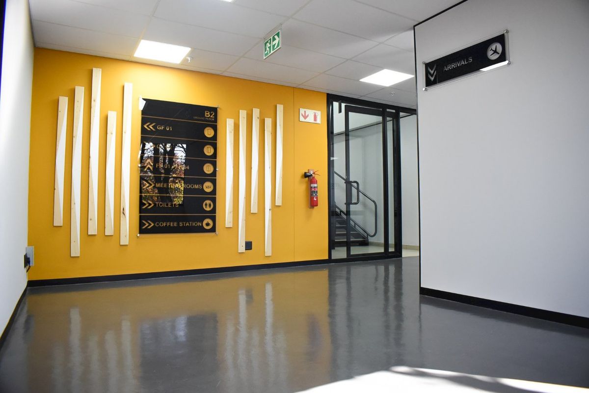 A modern commercial hallway featuring high-gloss epoxy flooring, recessed lighting, and clear directional signage leading to building amenities and arrival areas.
