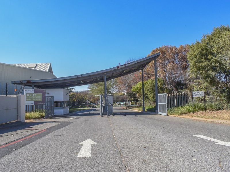 Commercial property entrance featuring a security gate, guard house, and metal canopy structure with asphalt driveway access.