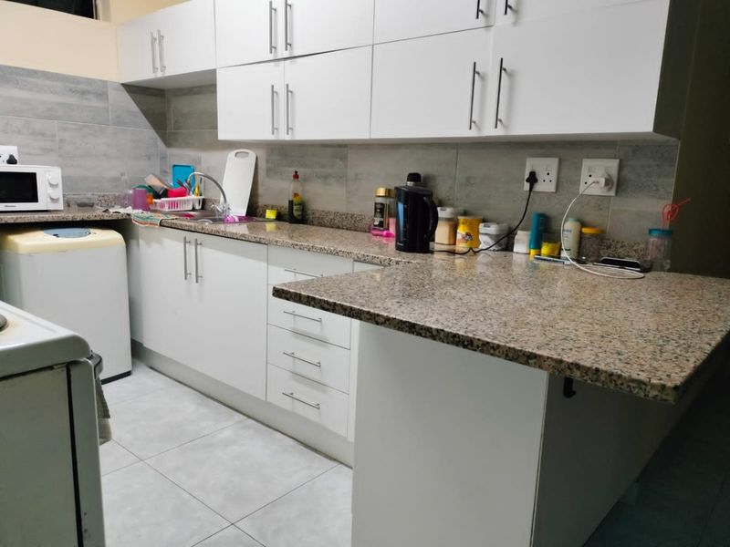 A functional kitchen featuring white cabinetry, granite countertops, tiled backsplash, and tiled flooring with a breakfast bar extension.