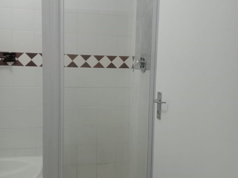 A functional bathroom featuring a shower enclosure with a glass door, tiled walls with a decorative border, and a built-in bathtub.