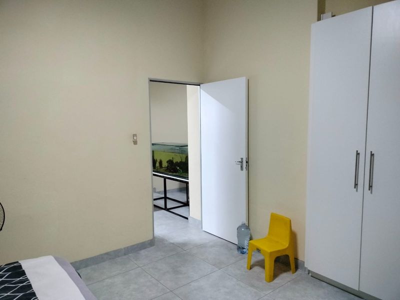 A bedroom featuring tiled flooring and a built-in white wardrobe, with an open doorway leading to an adjacent space.