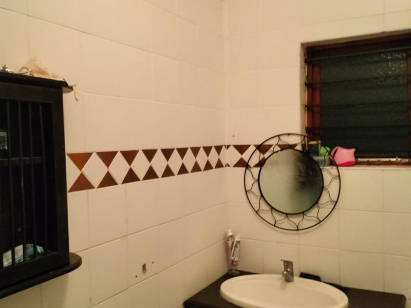 A functional bathroom featuring a dark vanity cabinet with an integrated sink, white wall tiles with a decorative border, and a louvre window.