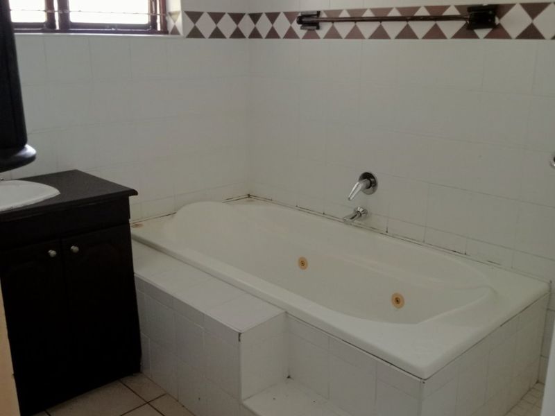 A functional bathroom featuring a built-in bathtub with tiled surround, a dark vanity cabinet, and neutral wall tiling.