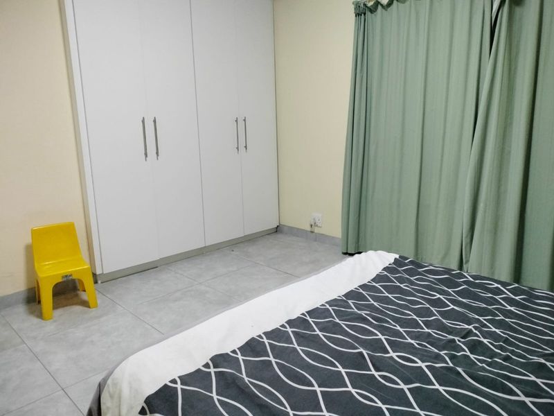 A bedroom featuring neutral tiled flooring and white built-in cupboards, providing functional storage space.