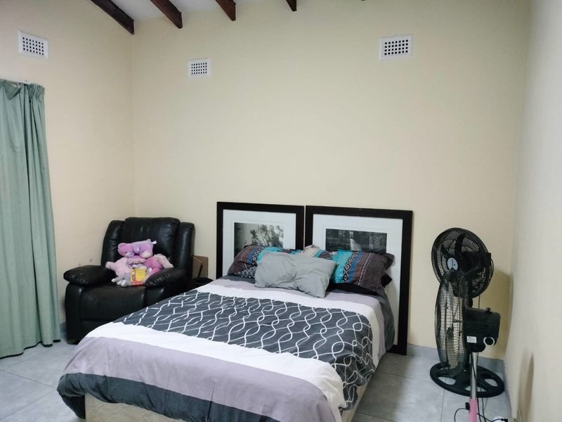 A bedroom featuring tiled flooring, exposed timber ceiling beams, and wall ventilation vents, providing a functional space with neutral wall finishes.