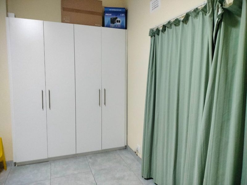 A bedroom featuring white built-in cupboards, tiled flooring, and a ceiling vent, providing a clean and functional space.