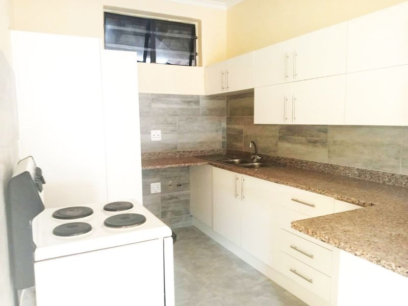 A clean, functional kitchen featuring white cabinetry, granite countertops, a tiled backsplash, and a freestanding electric stove.