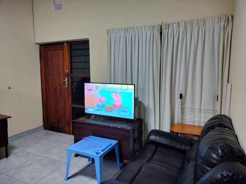 A living room area featuring tiled flooring, a wooden door, and neutral wall finishes, providing a functional space for relaxation.
