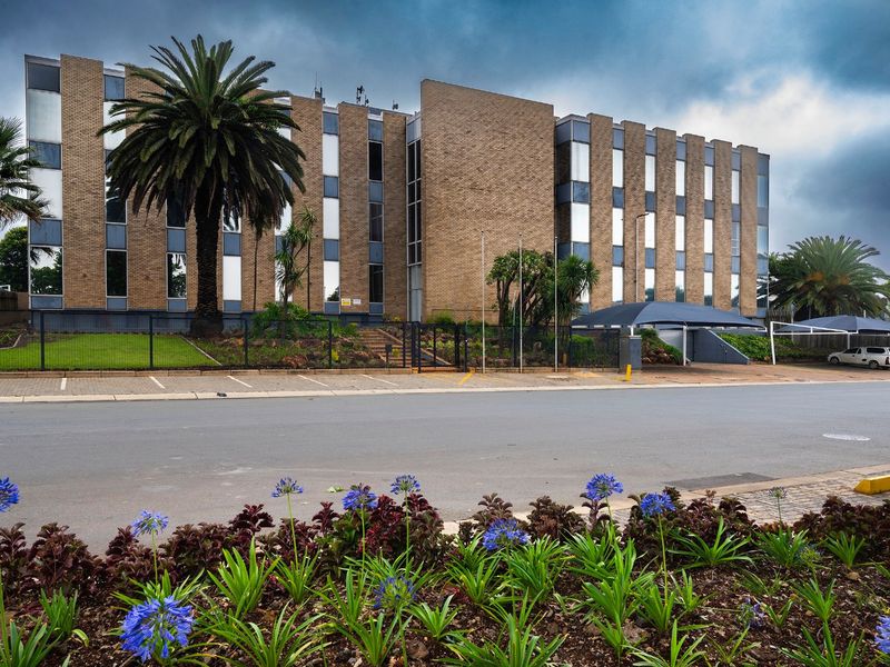 A multi-story commercial office building featuring a brick facade, large windows, and an adjacent paved parking area with covered carports.