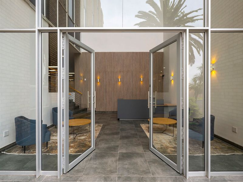 Modern commercial entrance lobby featuring floor-to-ceiling glass doors, tiled flooring, and elegant timber slat wall paneling with integrated lighting.