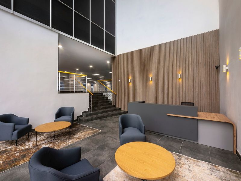 Modern commercial reception area featuring a sleek reception desk, decorative slatted timber wall paneling, tiled flooring, and a staircase with metal handrails.