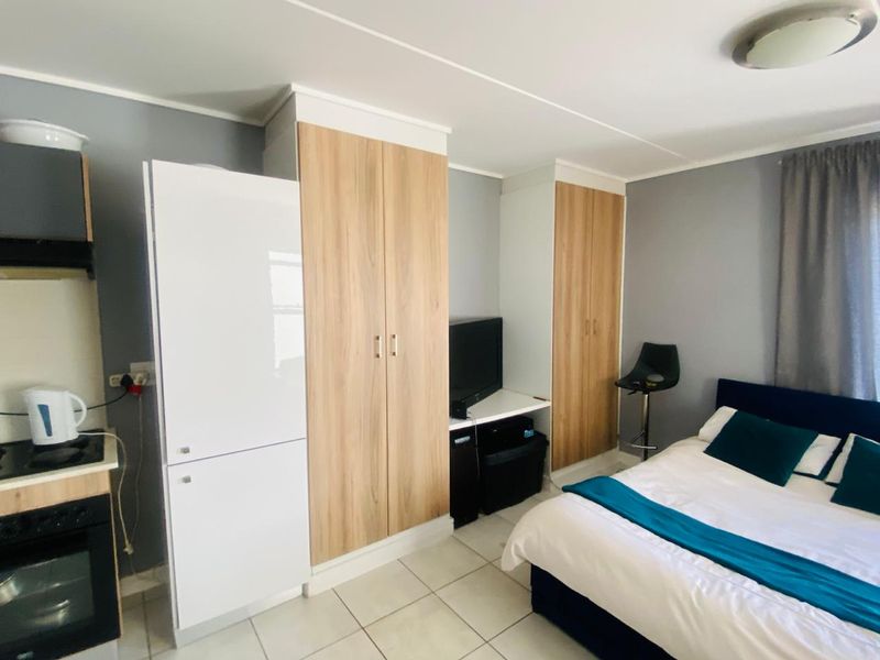 Compact open-plan studio space featuring a kitchenette with built-in oven, hob, and integrated cabinetry, alongside built-in storage cupboards and tiled flooring.