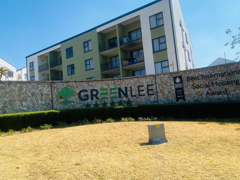 Front view of the Greenlee residential complex featuring a stone-clad boundary wall, landscaped grounds, and multi-story apartment blocks with balconies.