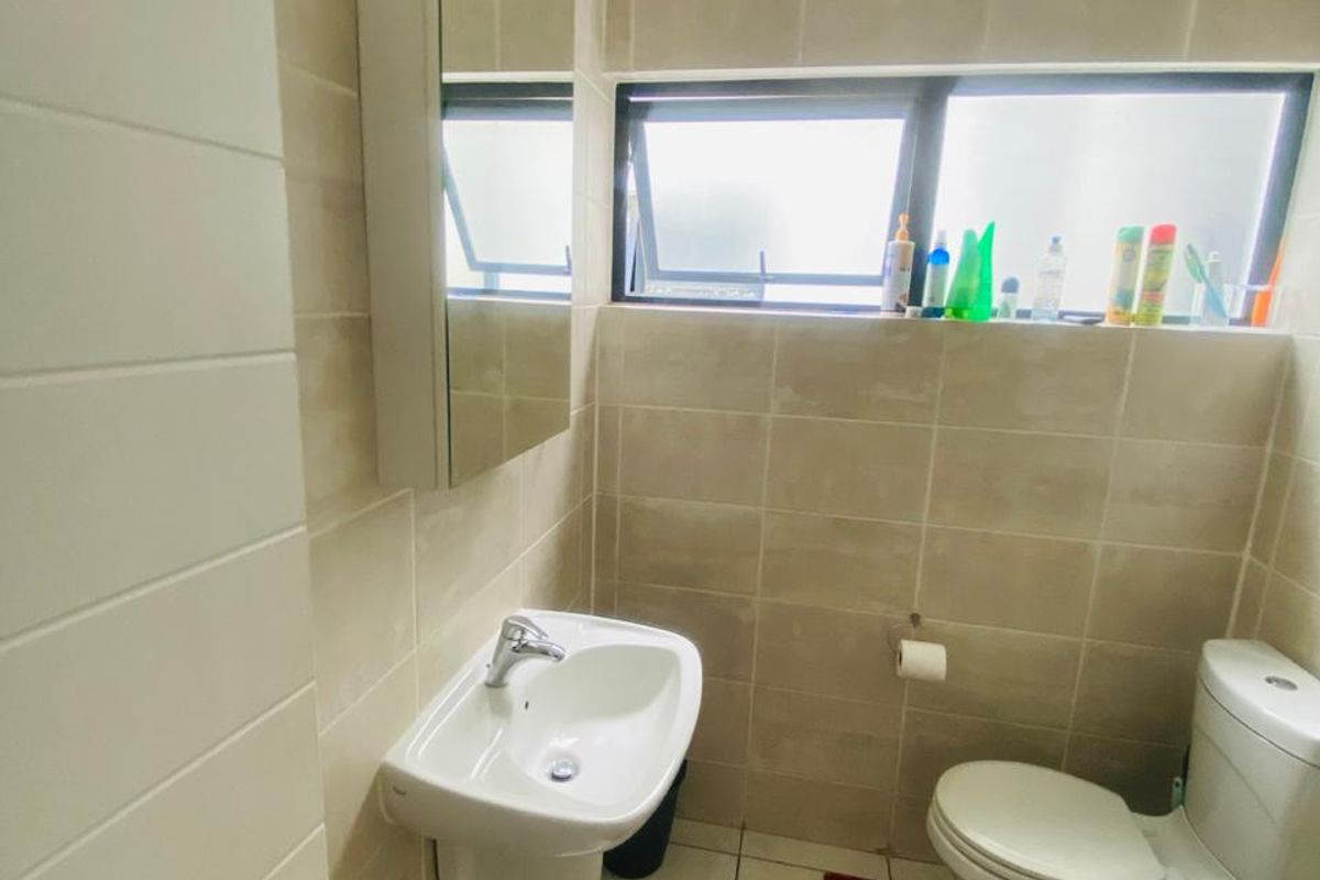 A compact, modern bathroom featuring tiled walls and floors, a wall-mounted basin, a mirror cabinet, and a standard toilet.