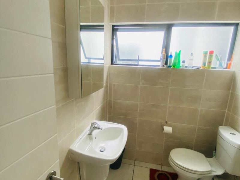 A compact, modern bathroom featuring tiled walls and floors, a wall-mounted basin, a mirror cabinet, and a standard toilet.