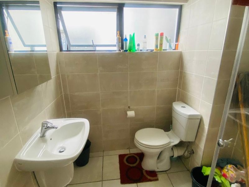 A functional bathroom featuring tiled walls and flooring, a wall-mounted basin, a toilet, and a glass-enclosed shower area.