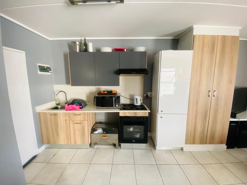 Compact kitchen featuring modern wood-look cabinetry, tiled flooring, built-in oven with hob, and an integrated extractor fan.