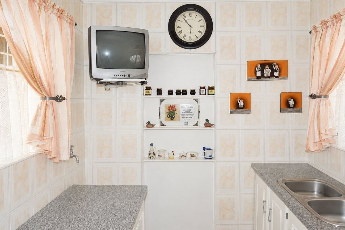 A functional kitchen area featuring tiled walls, laminate countertops, and a double bowl stainless steel sink with integrated shelving.