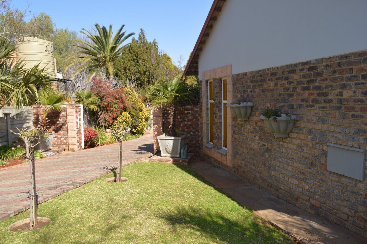 A well-maintained rear exterior view featuring a face brick facade, paved driveway, landscaped garden, and a water storage tank.