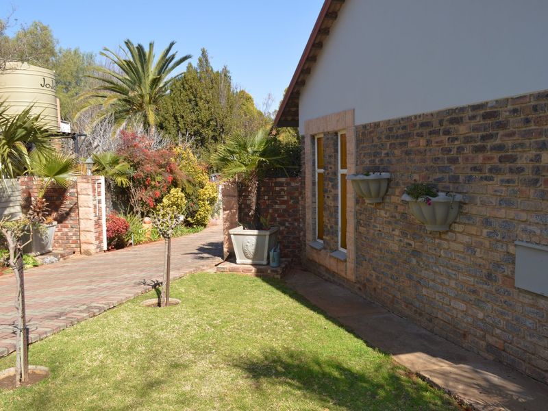 A well-maintained rear exterior view featuring a face brick facade, paved driveway, landscaped garden, and a water storage tank.