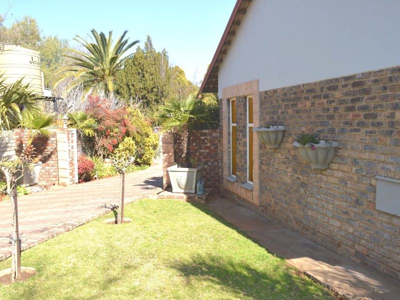 A well-maintained rear garden area featuring a face brick exterior wall, paved walkway, and established landscaping with a water storage tank.