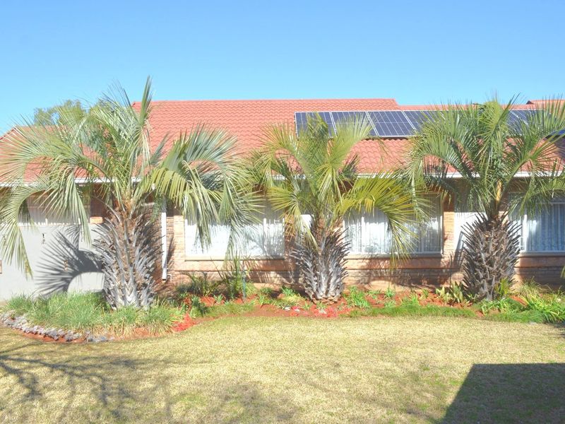 Rear view of the house featuring a tiled roof with integrated solar panels, brick exterior walls, and a well-maintained garden with mature palm trees.