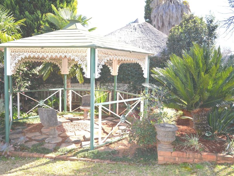 A charming garden gazebo featuring decorative wrought iron trim and stone paving, set within a landscaped backyard area.