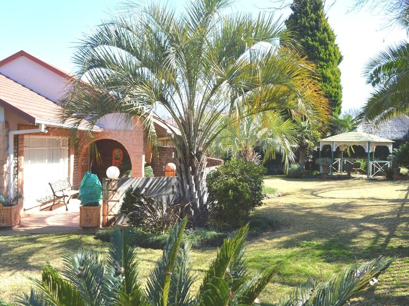 A spacious rear garden featuring a covered patio area, established palm trees, and a detached gazebo set within a well-maintained lawn.