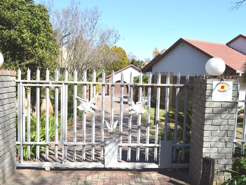 Front entrance view featuring a metal security gate, brick pillars, and a paved driveway leading to the main house.