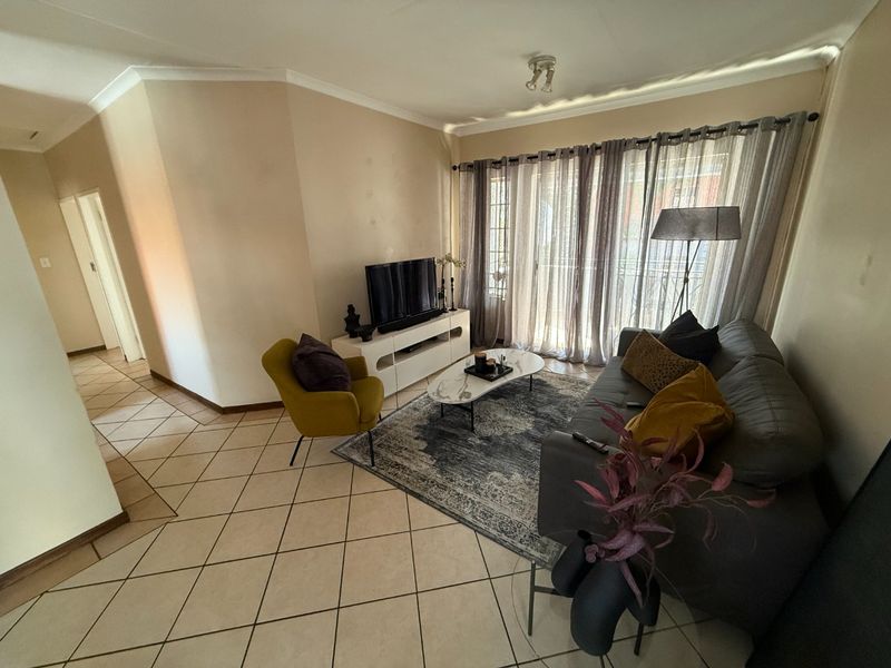 A living room featuring tiled flooring, cove cornicing, and a sliding glass door providing natural light.