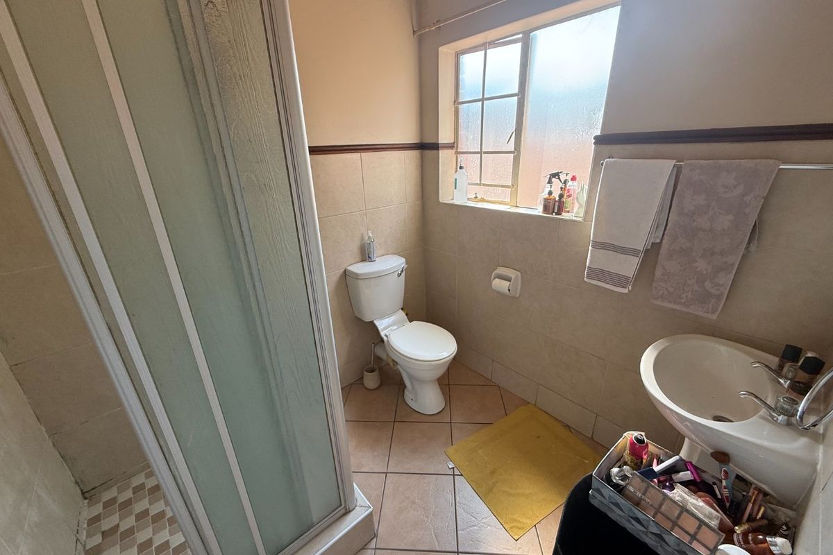 A functional bathroom featuring a shower enclosure, pedestal basin, and toilet with neutral wall and floor tiling.
