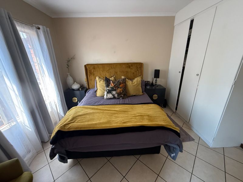 A bedroom featuring tiled flooring, a built-in wardrobe, and neutral wall tones, offering a functional space with potential for cosmetic updates.