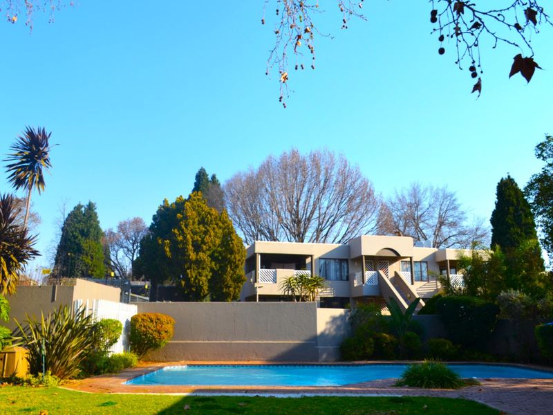 A view of the apartment complex exterior featuring a swimming pool, paved surround, and established garden area.