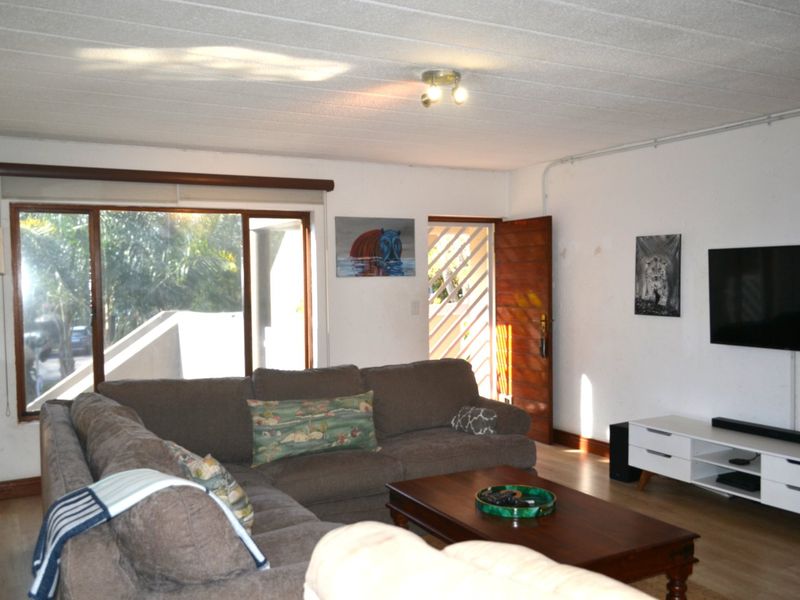 A living room featuring laminate flooring, a sliding glass door with security gate, and exposed electrical conduit along the wall.