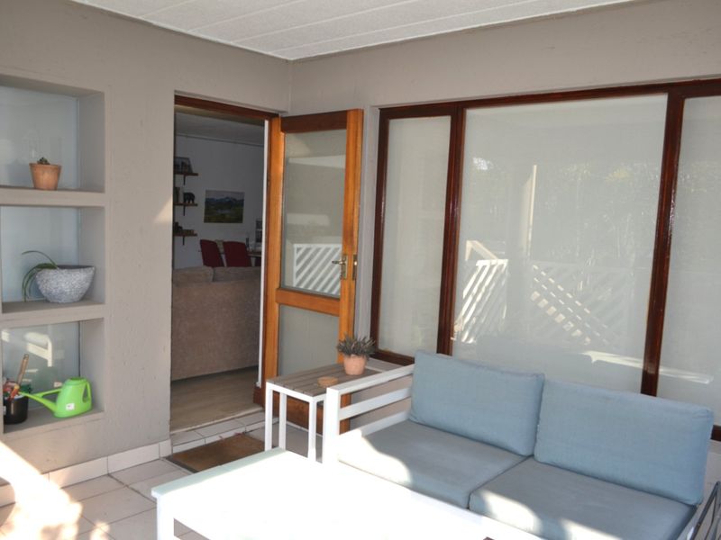 A covered patio area featuring built-in wall shelving, tiled flooring, and timber-framed access to the interior living space.