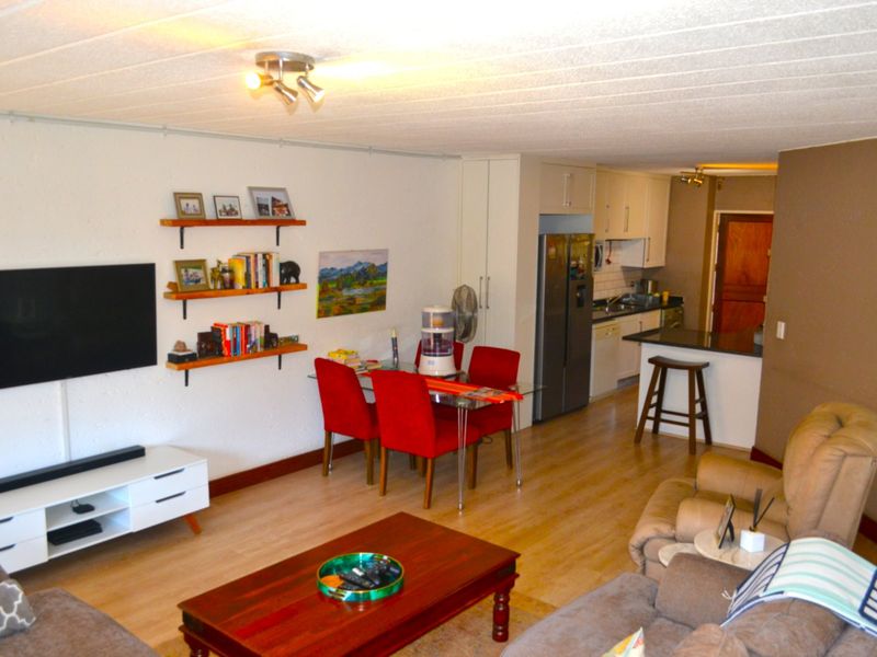 Open plan living and dining area featuring laminate flooring and a functional kitchen with built-in cabinetry and a breakfast bar.