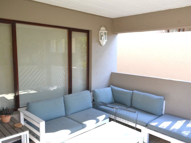 A covered balcony featuring tiled flooring, a solid masonry balustrade, and a wall-mounted light fixture, providing a private outdoor seating area.