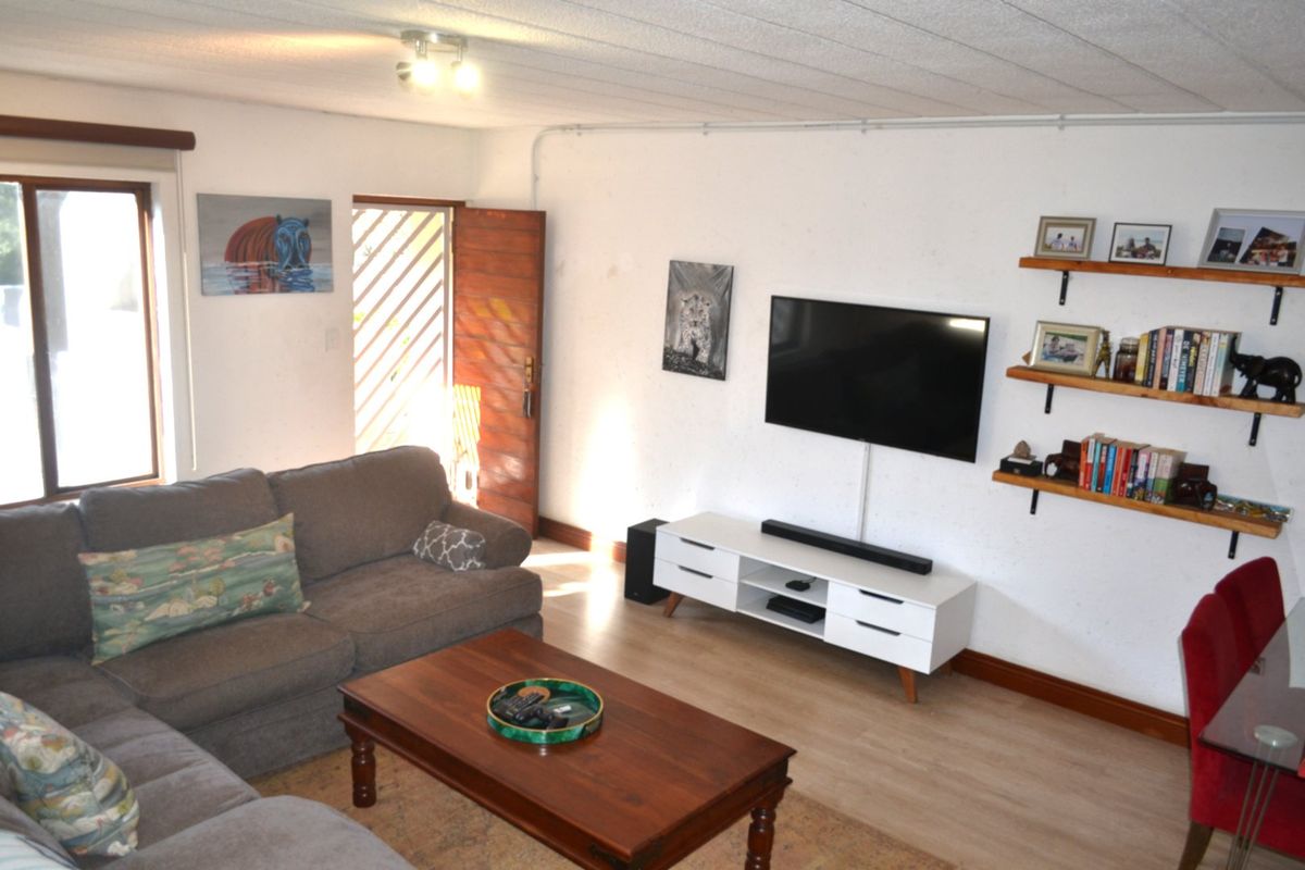 A living room featuring laminate flooring, a timber entrance door with security gate, and wall-mounted television setup with exposed electrical conduit.