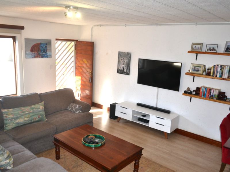 A living room featuring laminate flooring, a timber entrance door with security gate, and wall-mounted television setup with exposed electrical conduit.