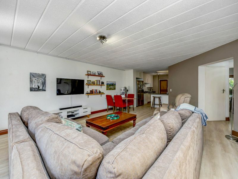 Open-plan living and dining area featuring laminate flooring, a panel ceiling, and a functional kitchen with a breakfast counter.