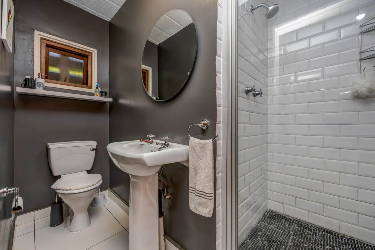 A compact bathroom featuring a pedestal basin, toilet, and a walk-in shower with white subway tiles and a mosaic floor.
