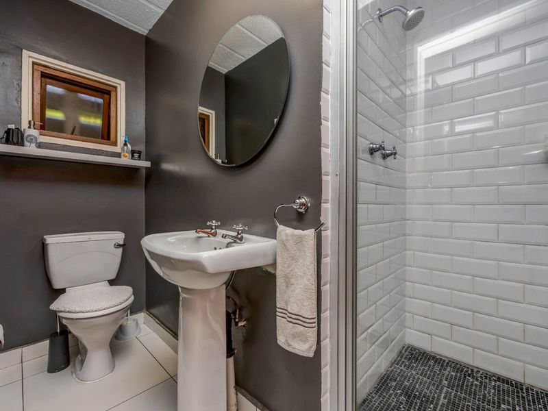 A compact bathroom featuring a pedestal basin, toilet, and a walk-in shower with white subway tiles and a mosaic floor.