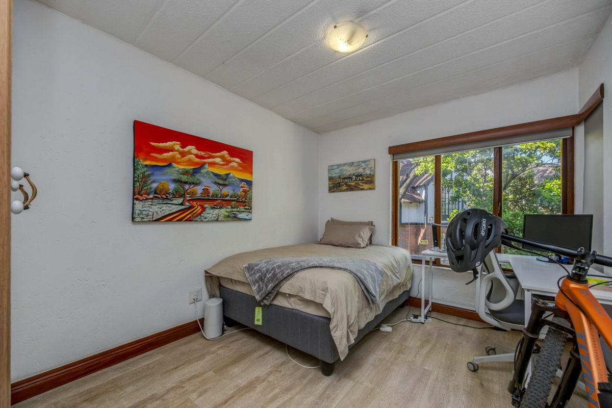 A functional bedroom featuring laminate flooring, timber window frames, and a ceiling light fixture, offering a comfortable space with natural light.