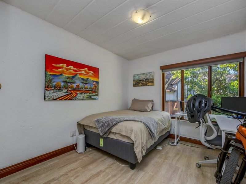 A functional bedroom featuring laminate flooring, timber window frames, and a ceiling light fixture, offering a comfortable space with natural light.