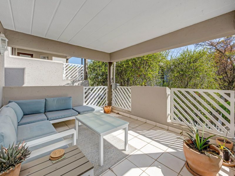 A covered balcony featuring tiled flooring and white railings, offering a pleasant outdoor space with views of surrounding greenery.