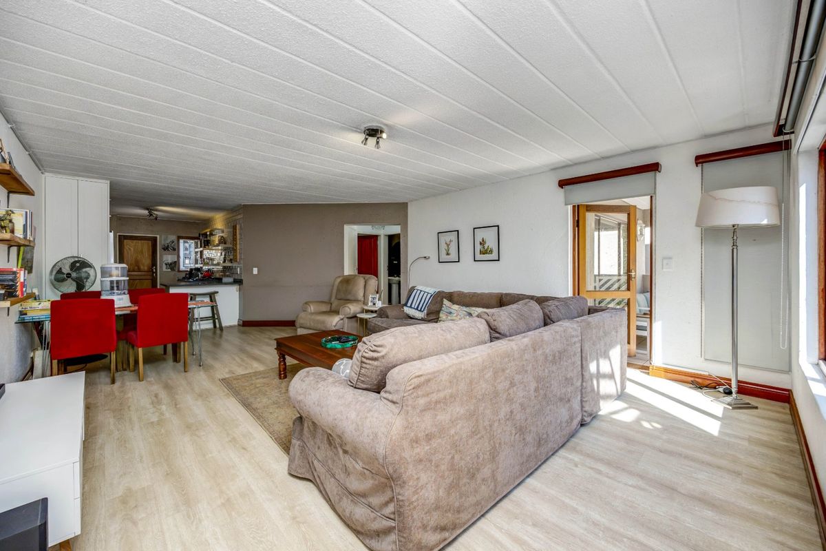 Spacious open-plan living and dining area featuring light laminate flooring, a functional kitchen breakfast bar, and direct access to an adjoining room.