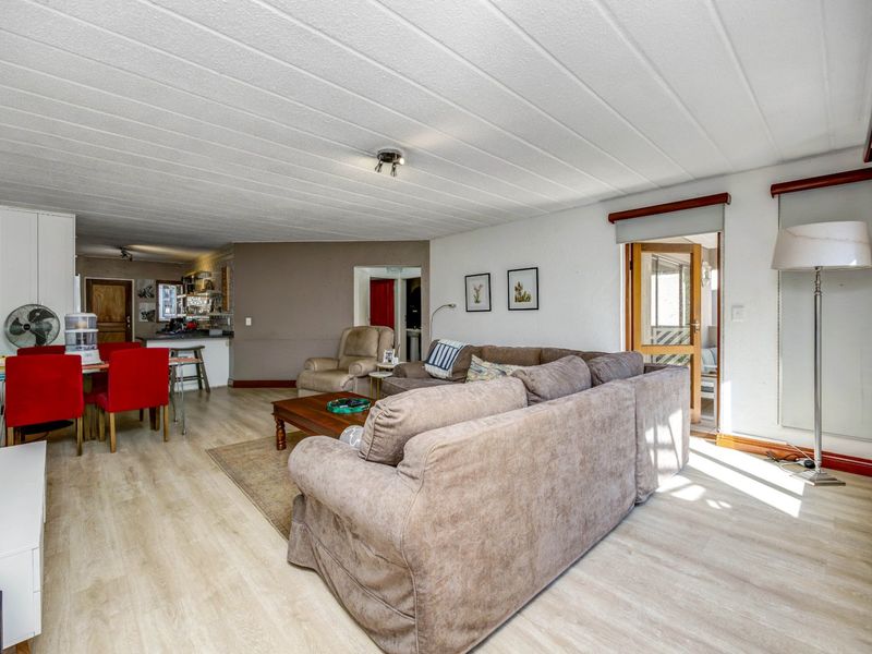 Spacious open-plan living and dining area featuring light laminate flooring, a functional kitchen breakfast bar, and direct access to an adjoining room.