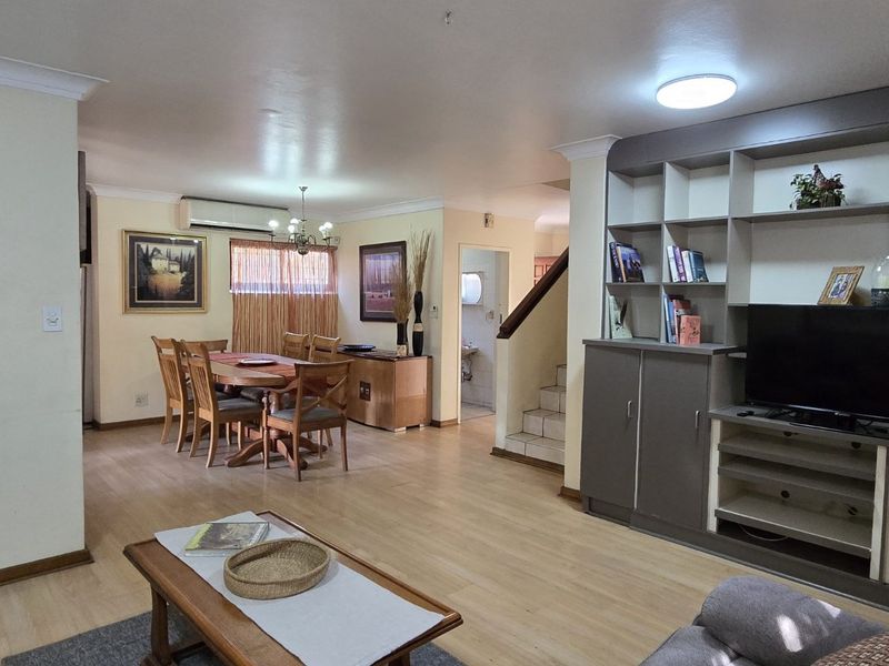 Open-plan living and dining area featuring laminate flooring, a built-in media shelving unit, and access to the staircase.